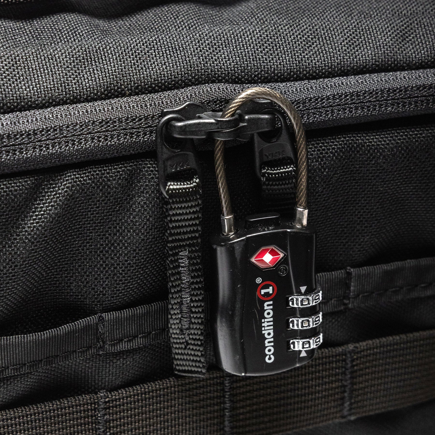 Close-up of a black Lone Star 2 Pistol Bag with a combination lock securing the zipper, attached to a textured black fabric surface.