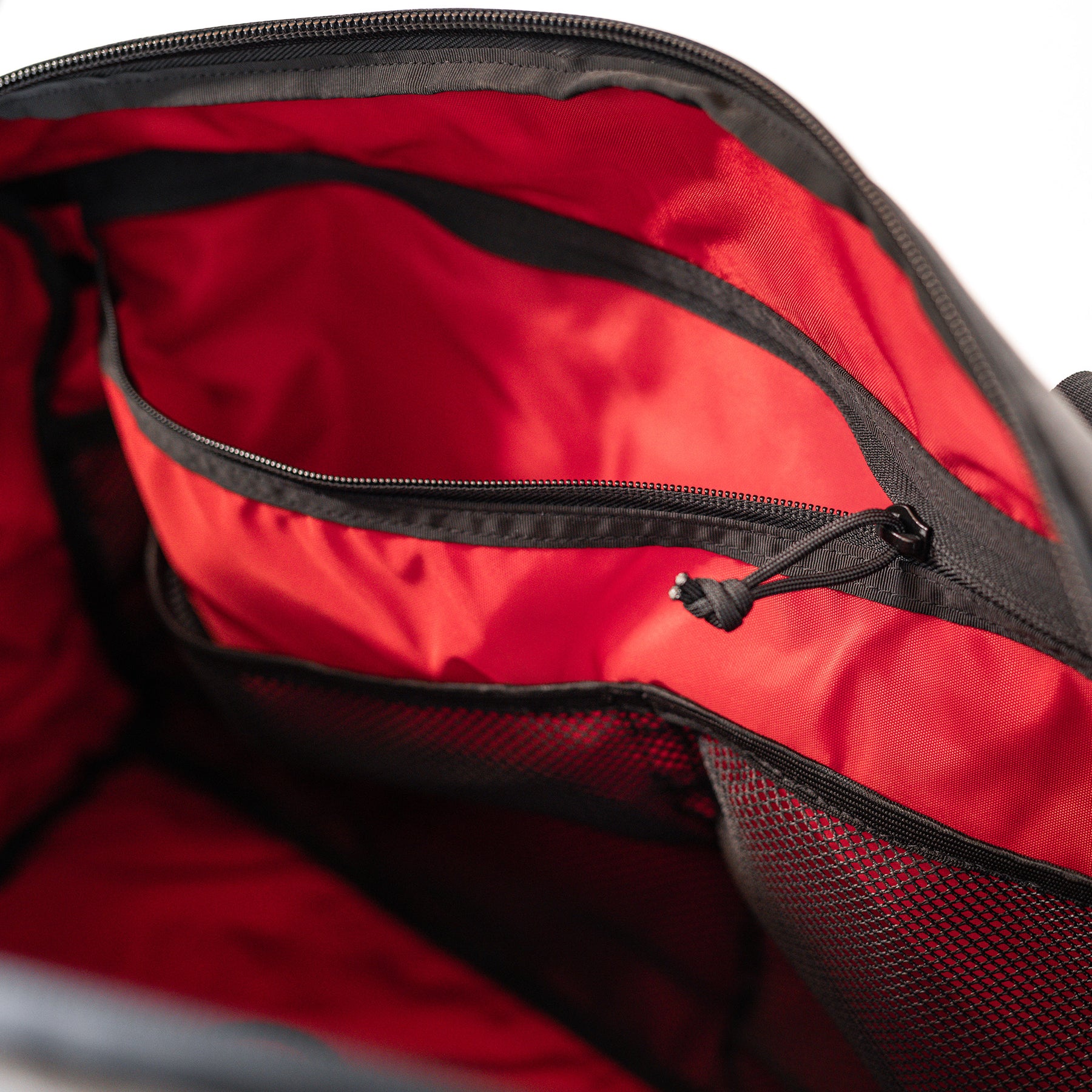 Interior view of the GOBAG Waxed Canvas Duffle showing red lining, multiple zippered compartments, and mesh pockets.