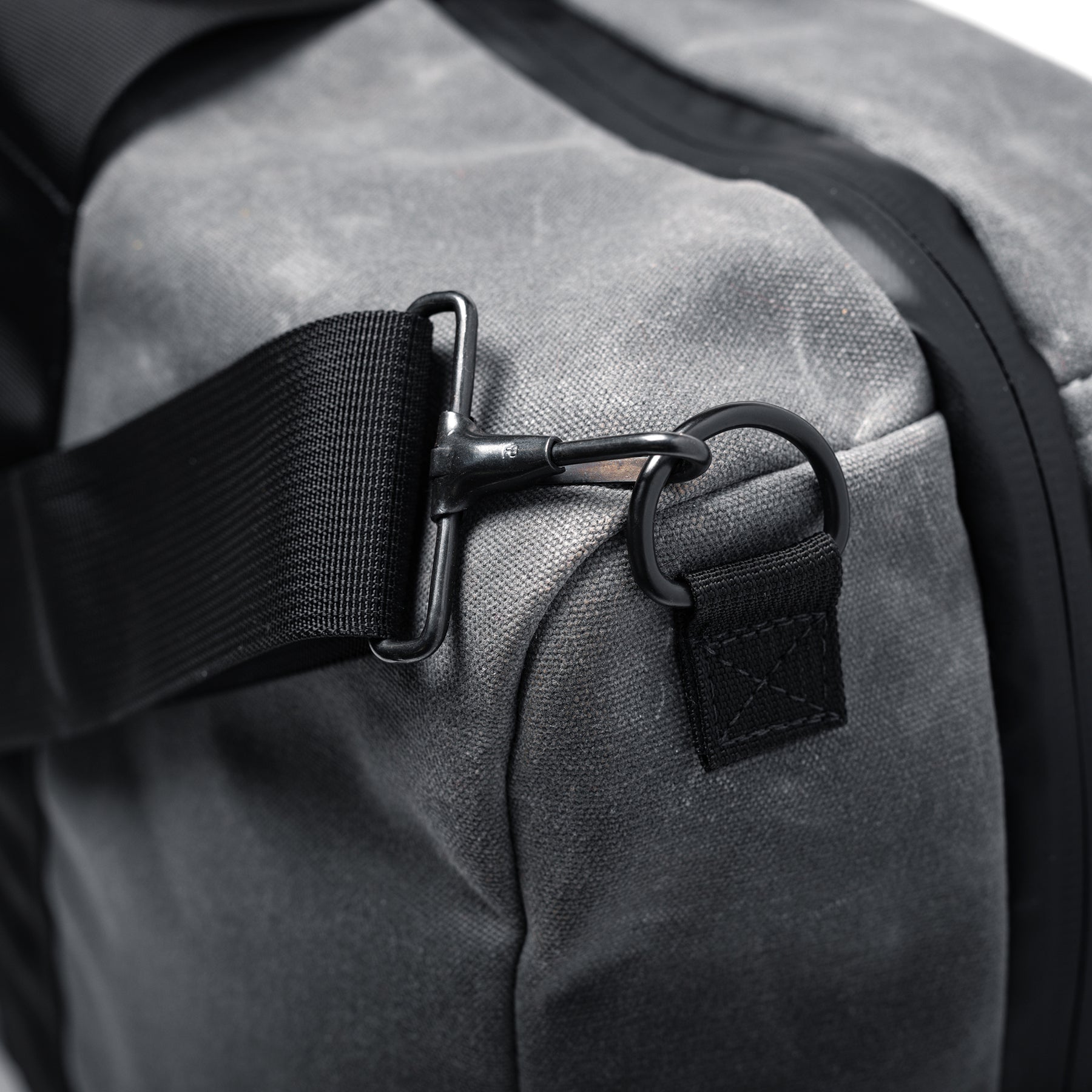 Close-up of the GOBAG Waxed Canvas Duffle with black strap and metal hook attachment on gray, durable, waxed canvas material.