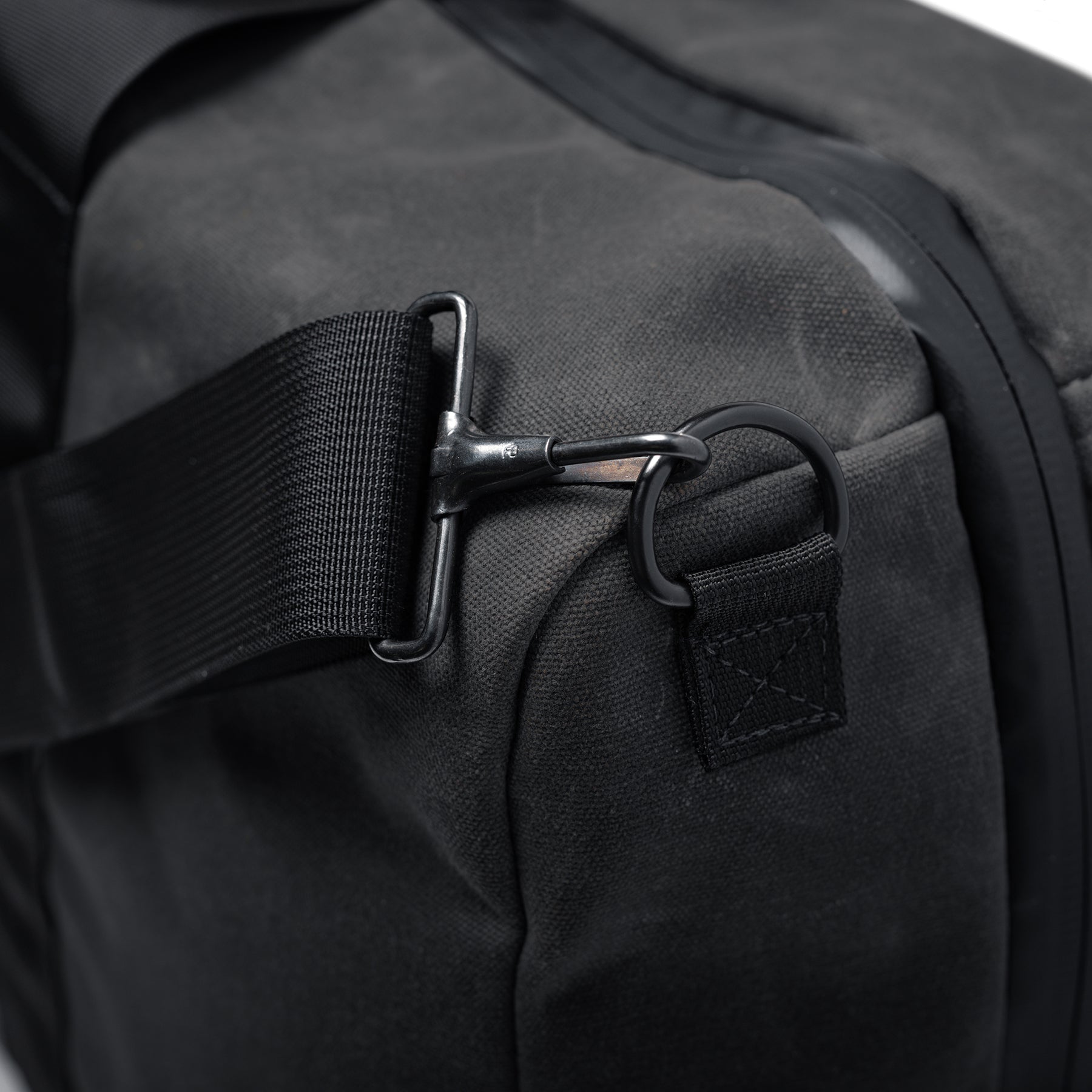 Close-up of the GOBAG Waxed Canvas Duffle with black strap and metal hook attachment on durable black fabric.