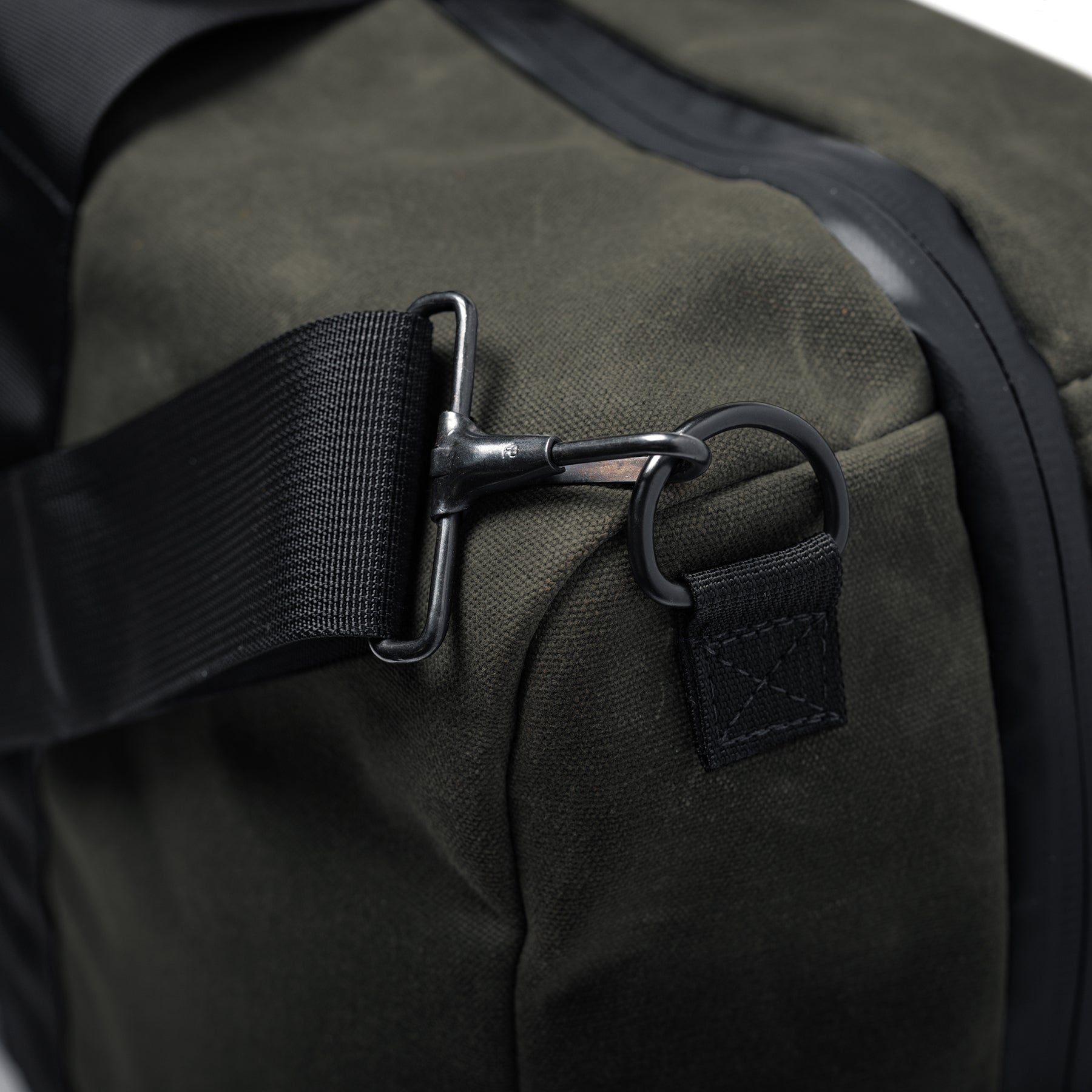 Close-up of the GOBAG Waxed Canvas Duffle with black strap and metal hook attachment on olive-green waxed canvas fabric.