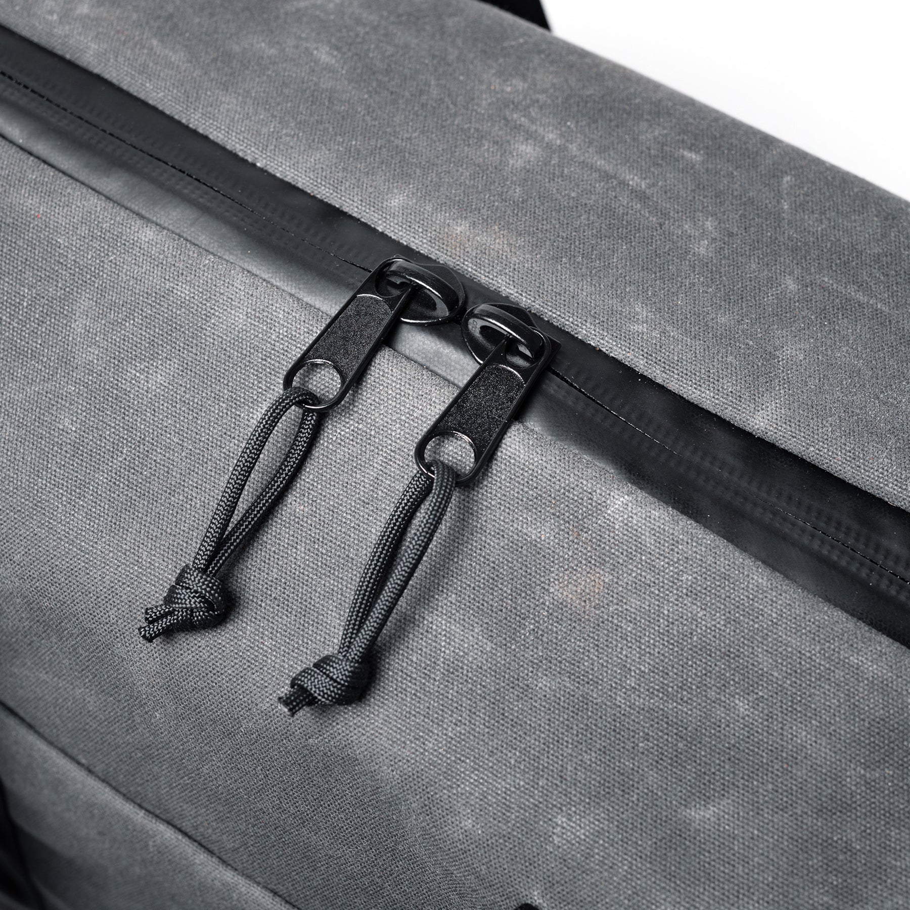 Close-up of the GOBAG Waxed Canvas Duffle with black zipper pulls and durable cord pulls on a grey waxed canvas bag.