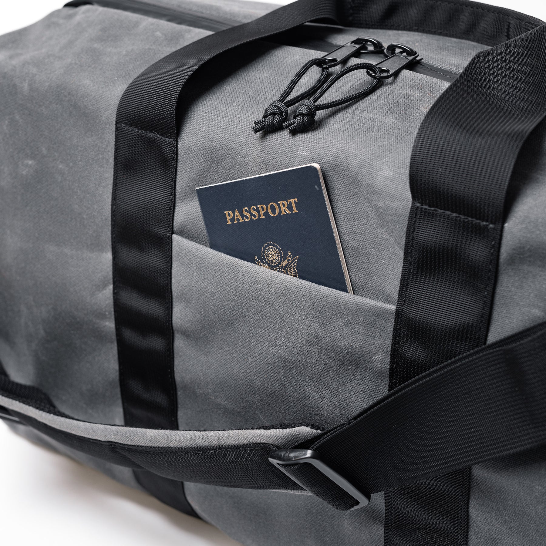 The GOBAG Waxed Canvas Duffle bag with a passport in the front pocket, featuring durable waxed canvas material and black straps.