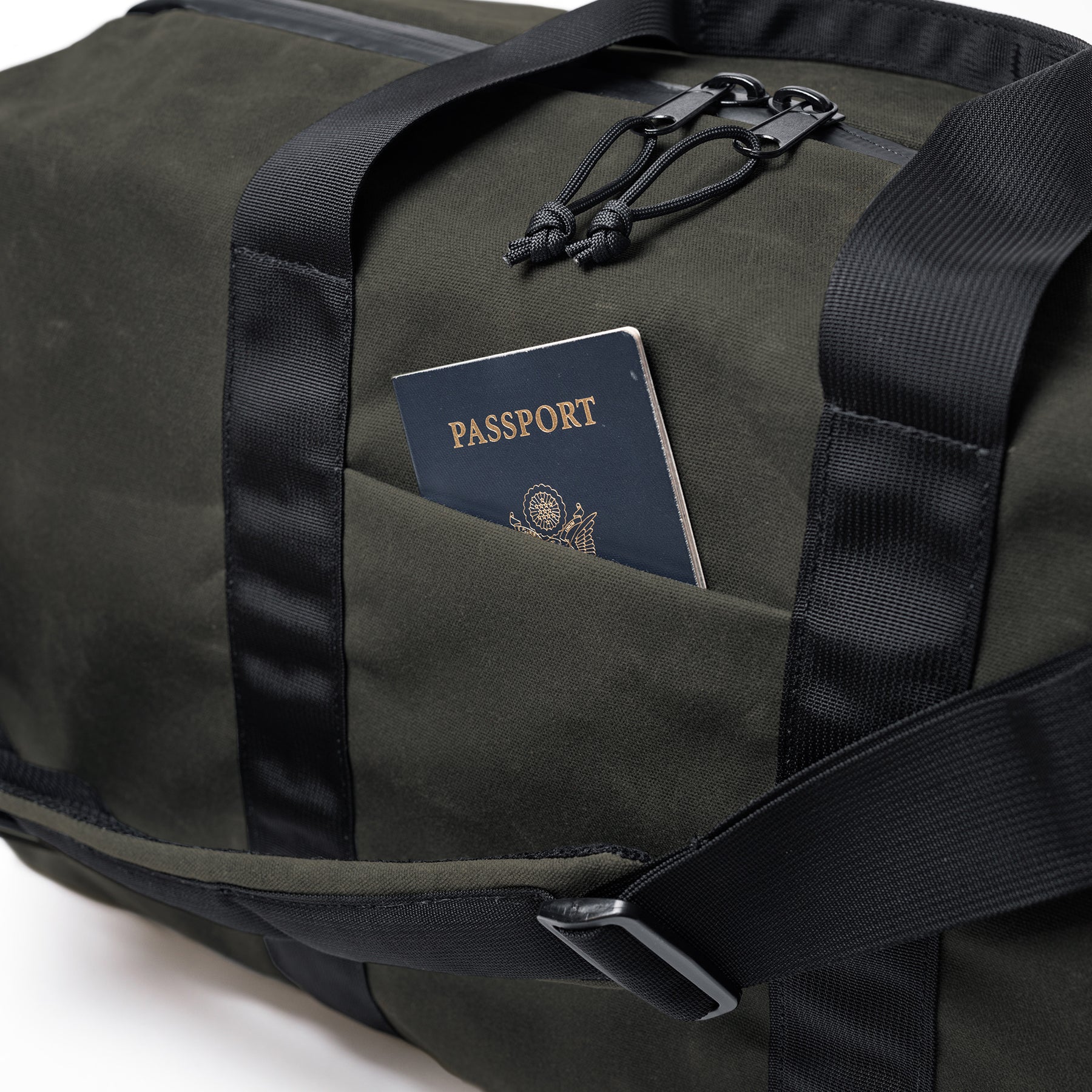 The GOBAG Waxed Canvas Duffle bag with a passport in the front pocket, featuring durable waxed canvas material and black straps.