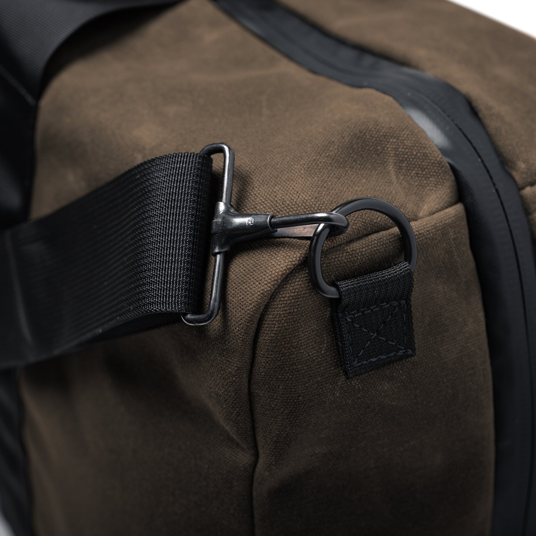 Close-up of the GOBAG Waxed Canvas Duffle with black strap and metal hook attachment on brown waxed canvas fabric.
