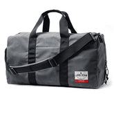 Gray waxed canvas duffle bag with black straps, handles, and adjustable shoulder strap, featuring a red and white label.