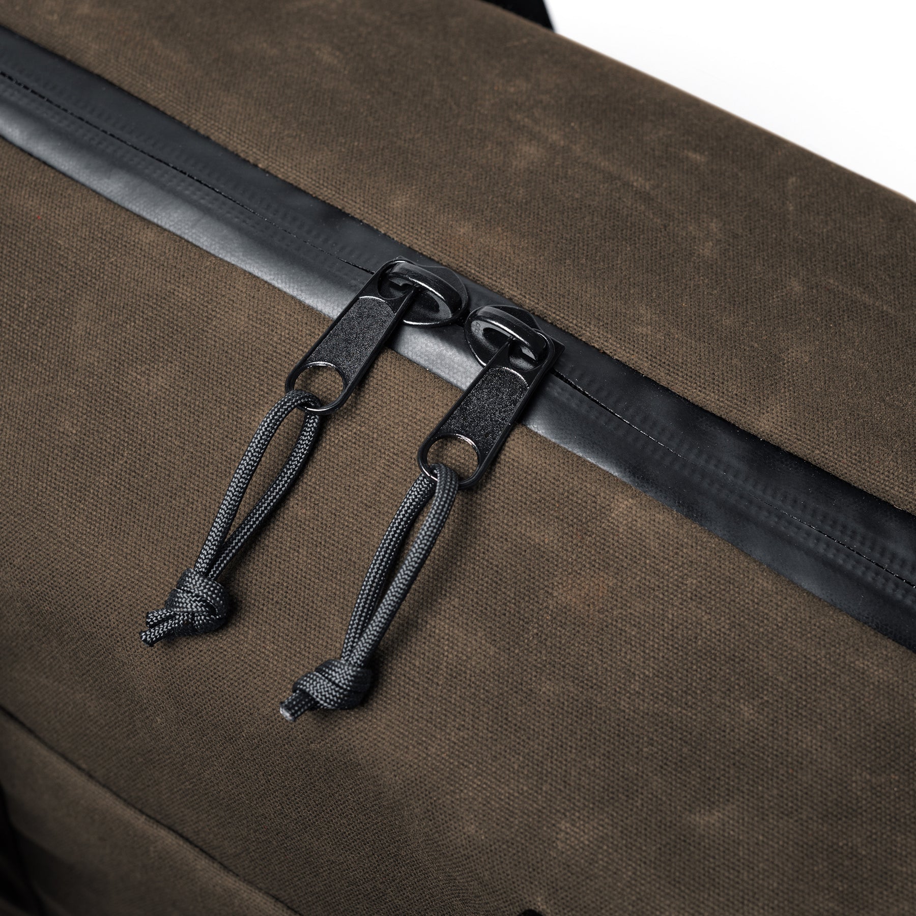 Close-up of the GOBAG Waxed Canvas Duffle with dual black zipper pulls and cord pulls on a brown textured fabric bag.