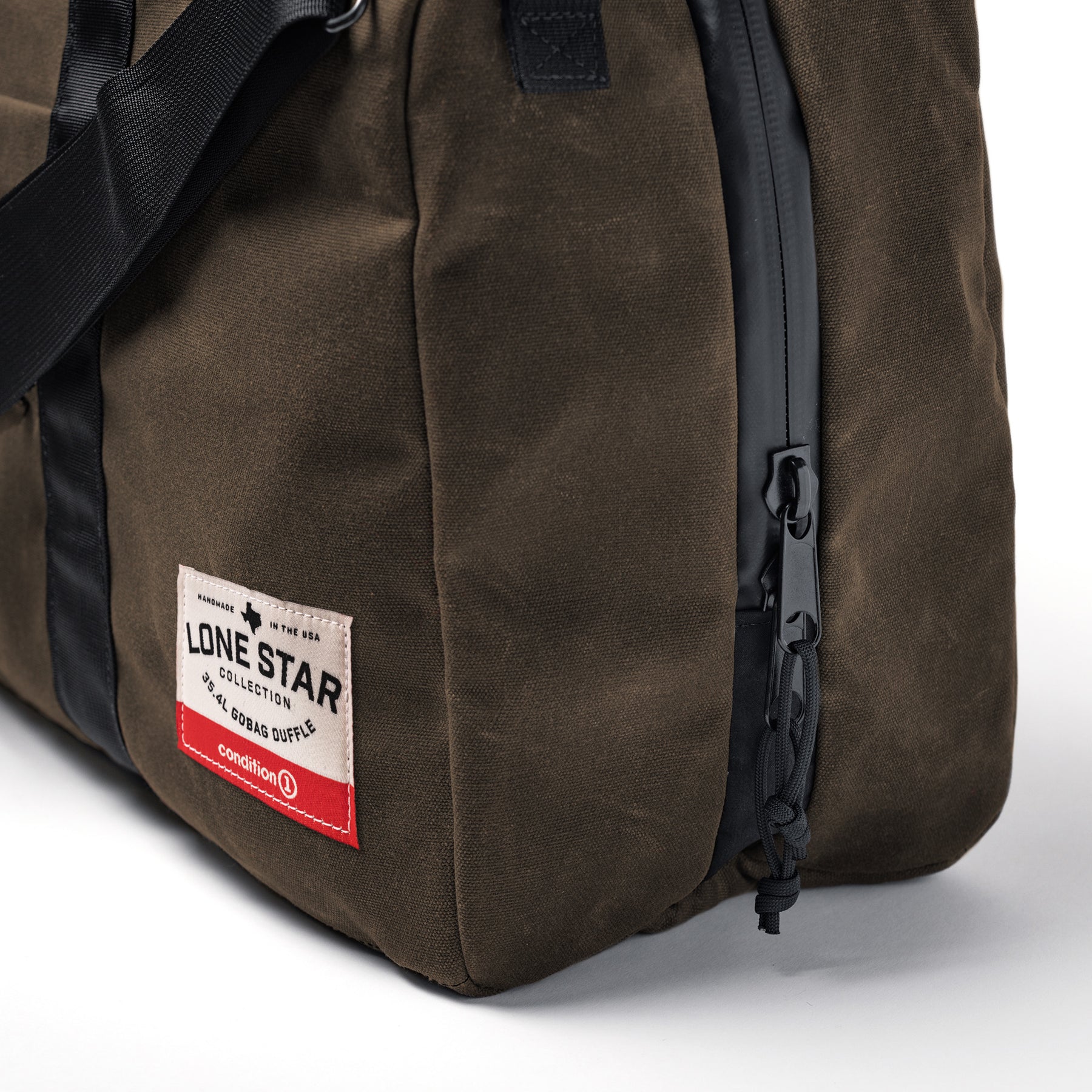 Close-up of the brown waxed canvas duffle bag with black zipper, strap, and a white label reading "Lone Star Collection.