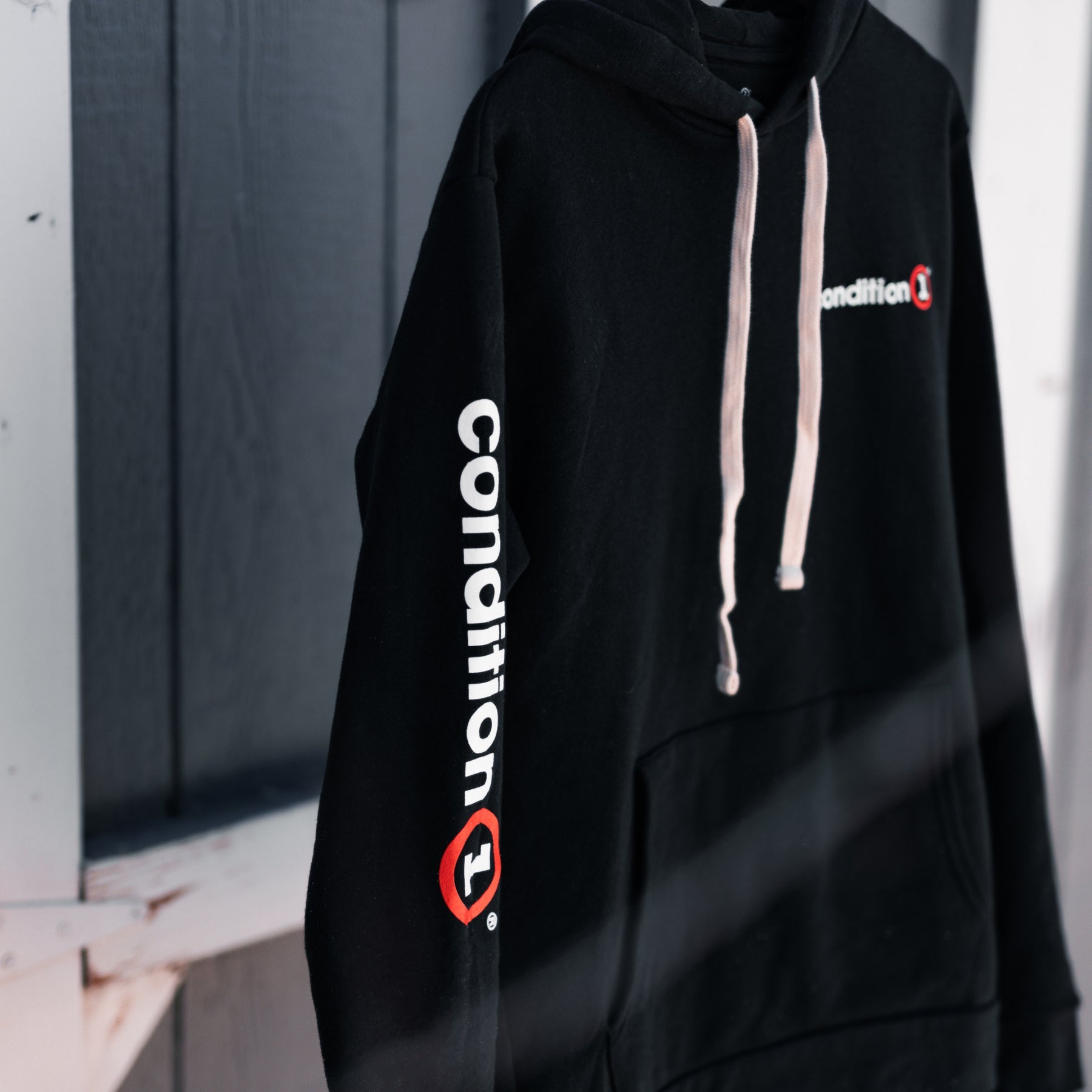 Black hoodie with "Condition" logo on chest and sleeve, featuring white and red accents, and beige drawstrings.