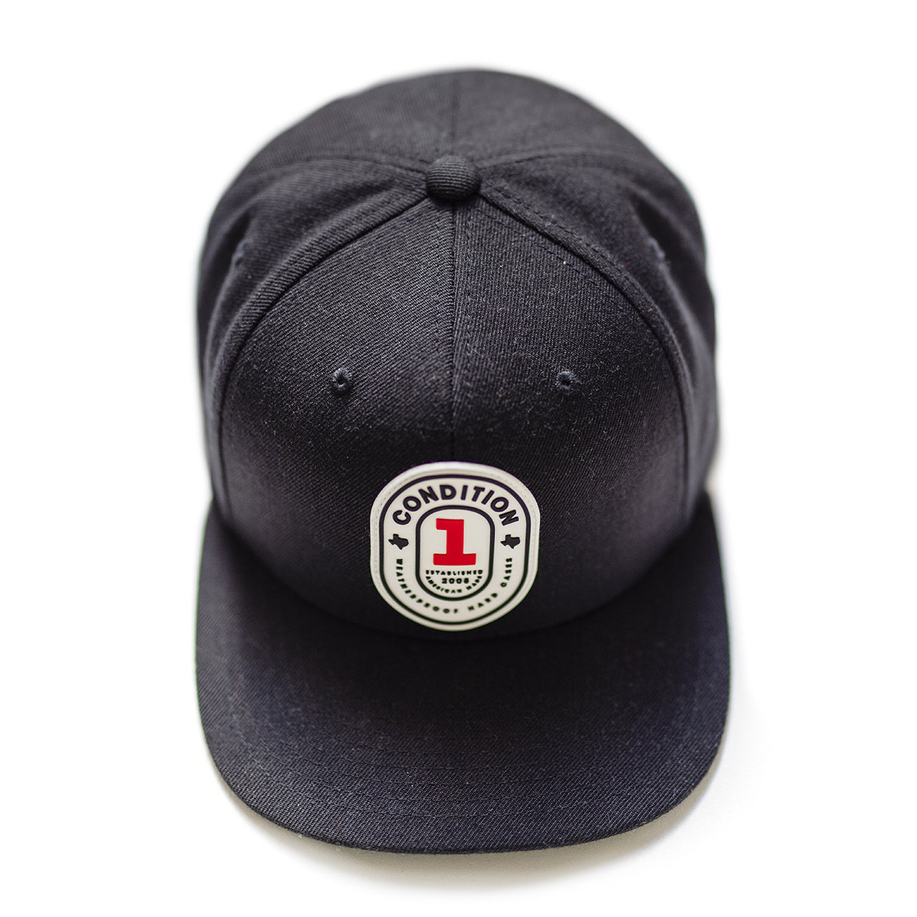 Black snapback cap with a front patch reading "Condition + The One" and a red number "1" logo, featuring a curved brim and adjustable strap.