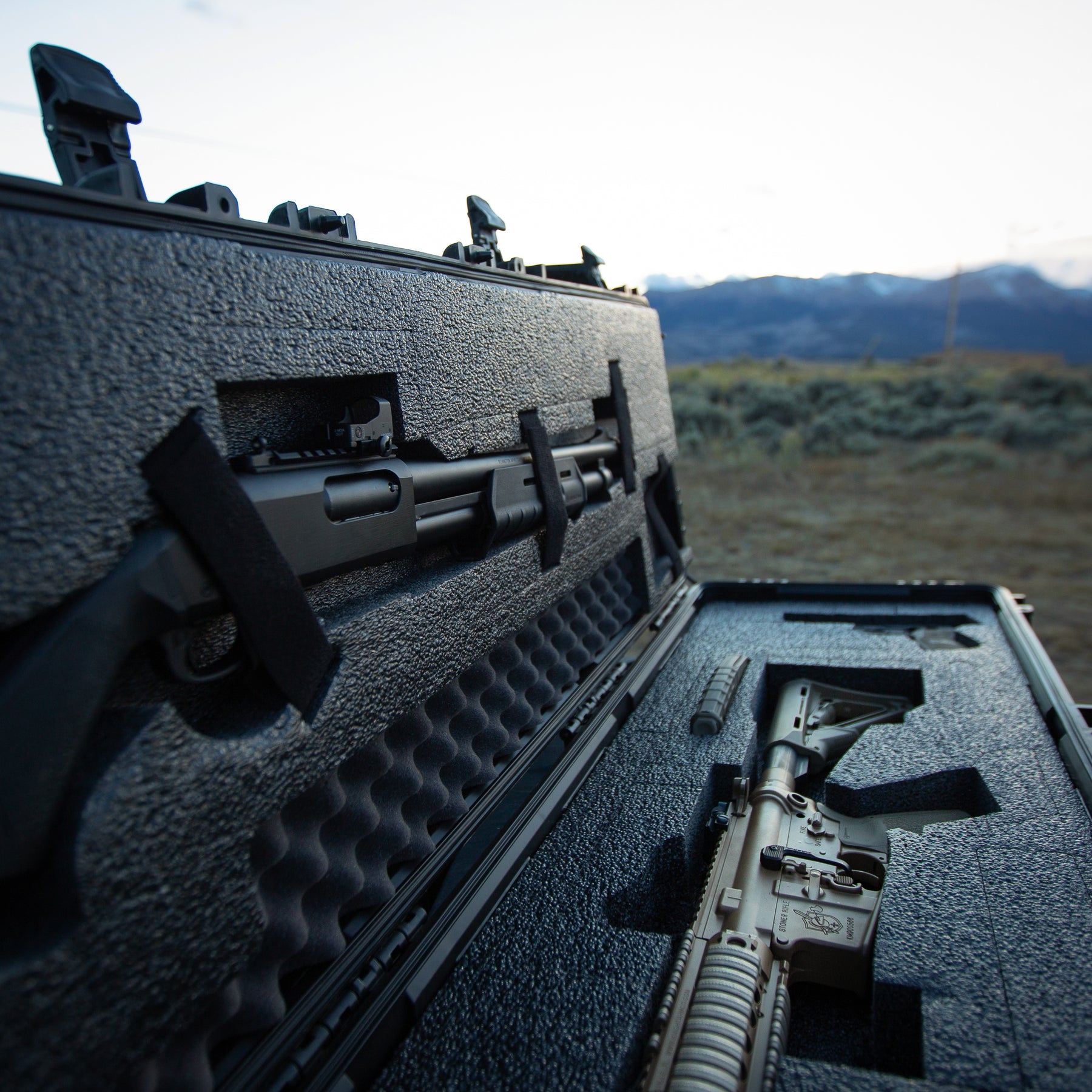 A 55-inch black gun case with foam interior, holding a rifle and accessories, outdoors with mountains in the background.