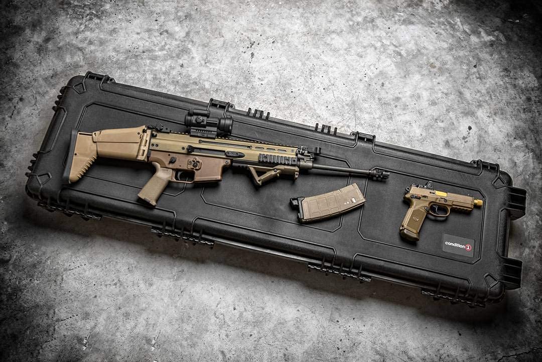 A 45-inch long black hard case with a rifle, a magazine, and a handgun placed on top, all arranged on a concrete floor.