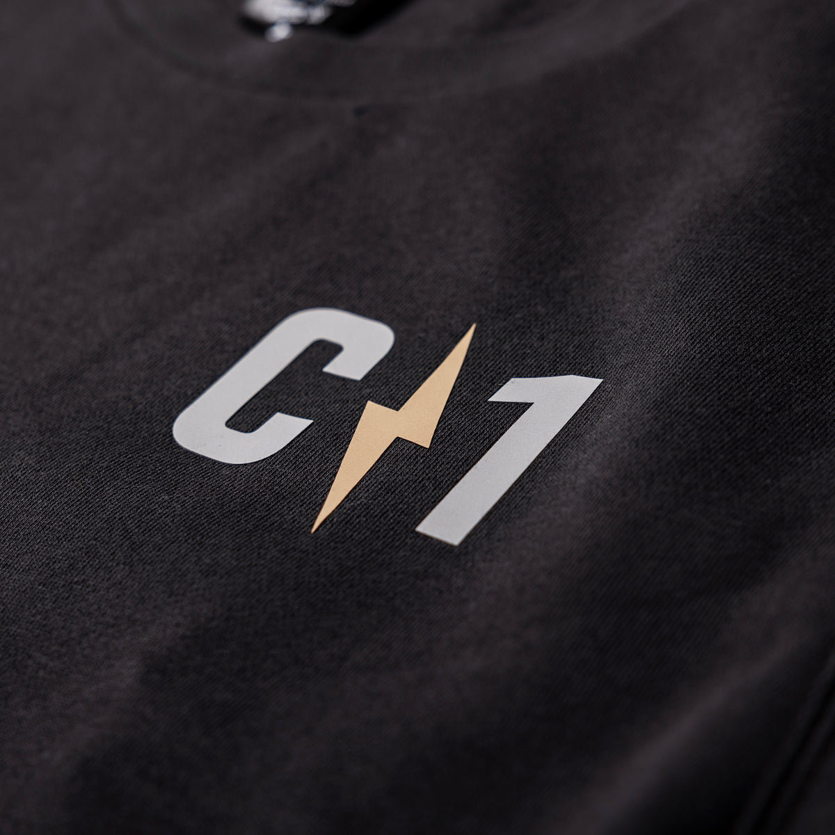 Close-up of a black crew sweatshirt featuring a prominent C1 logo with a lightning bolt design in gold and white.