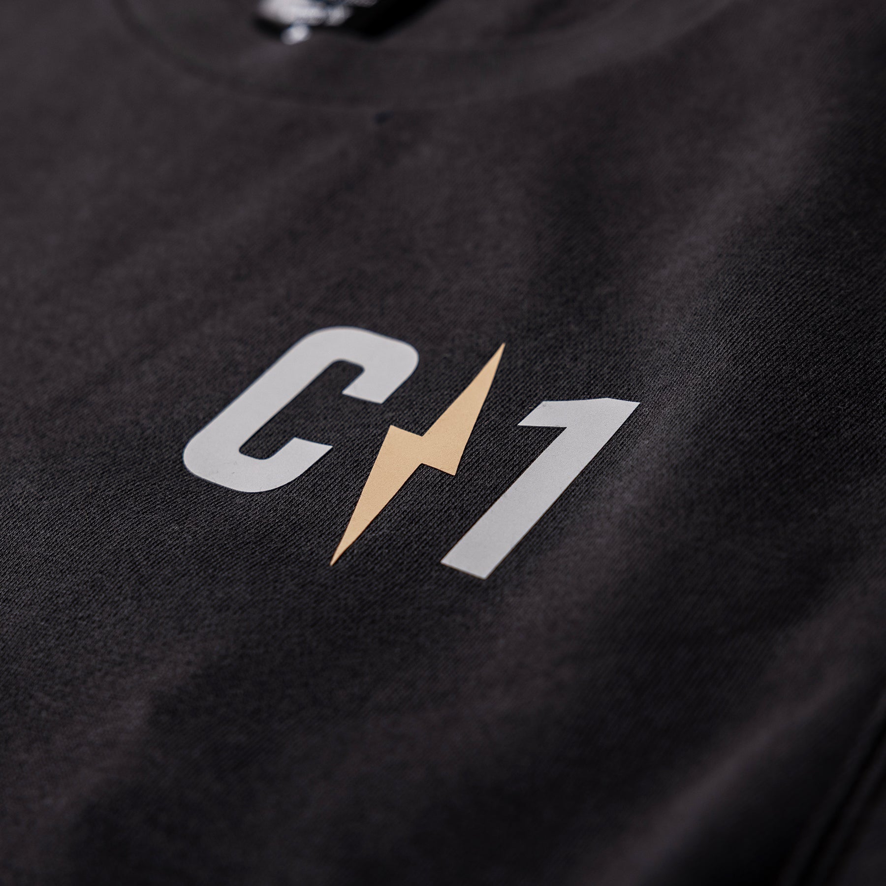 Close-up of a black crew sweatshirt featuring a prominent C1 logo with a lightning bolt design in gold and white.