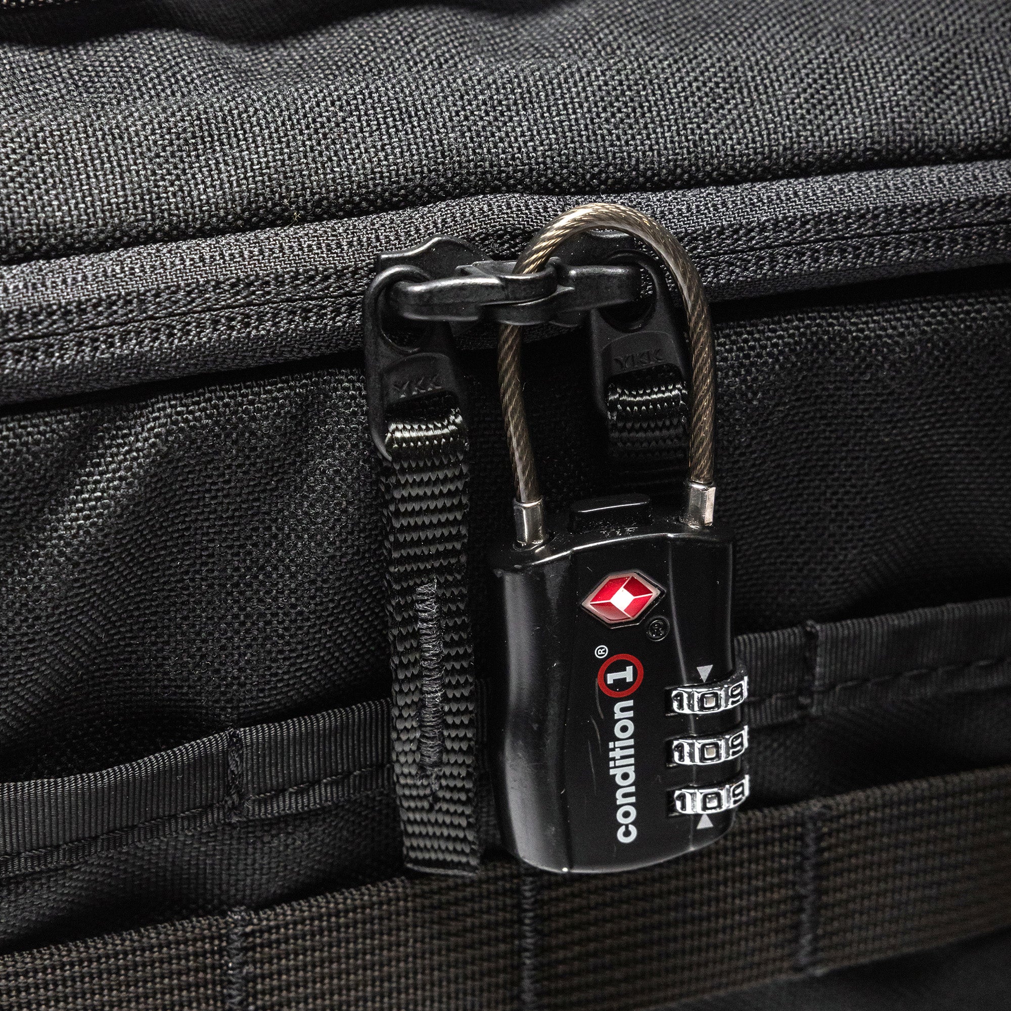 Close-up of a black Lone Star 2 Pistol Bag with a combination lock securing the zipper, attached to a textured black fabric surface.