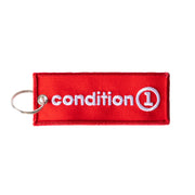 Red fabric keychain with white embroidered "Condition 1" logo and a metal keyring attachment.